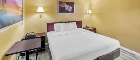 Una habitación de hotel con cama, escritorio, sillas y dos lámparas fijadas a la pared.