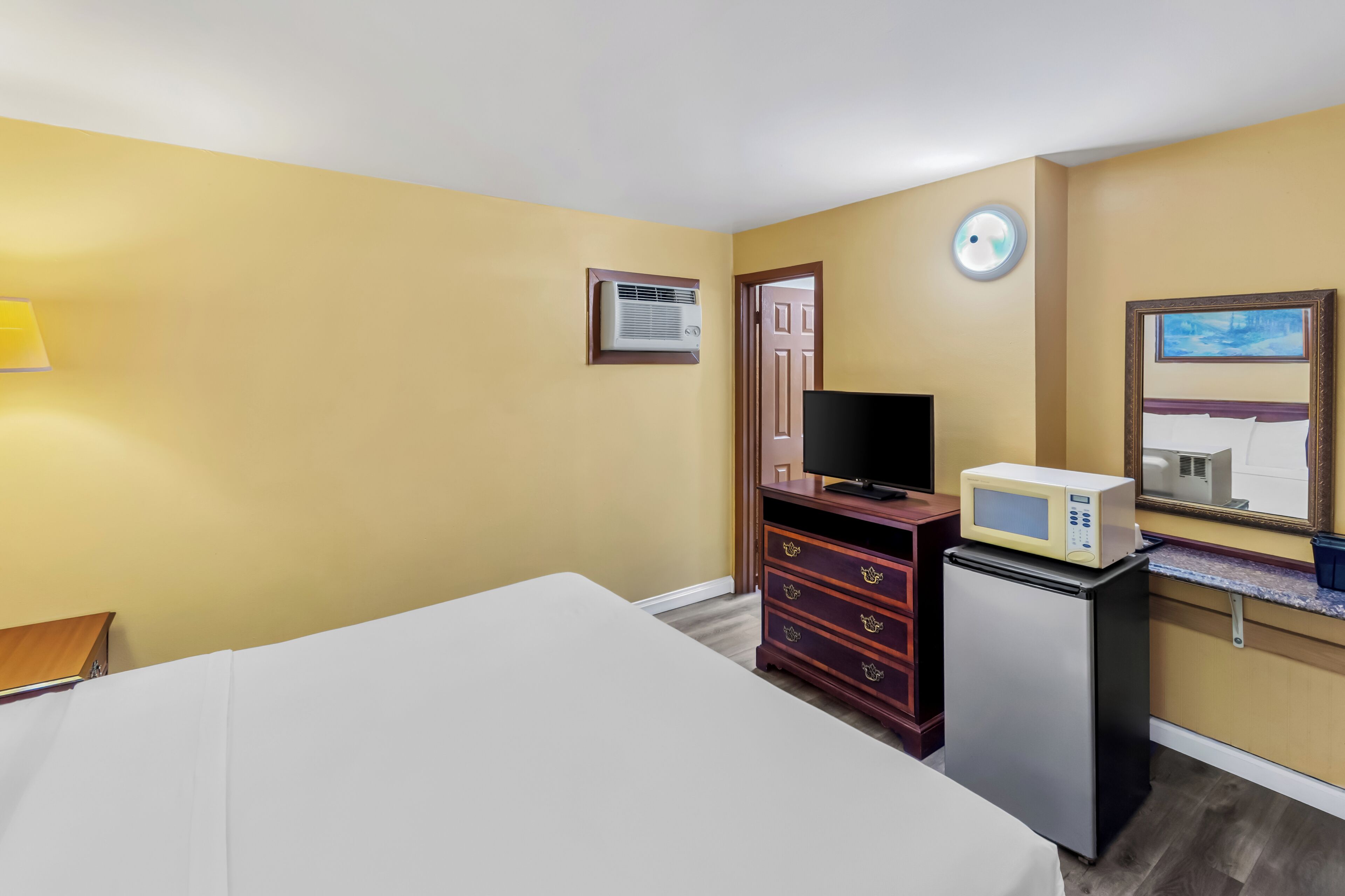 A hotel room with a bed, a TV, a microwave, a small fridge, a dresser, and a door.