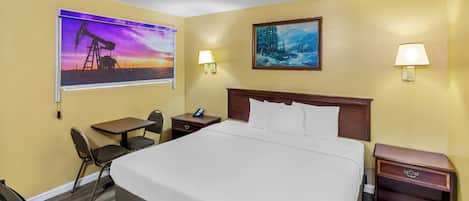A hotel room with a bed, a desk, two chairs, a nightstand, and two wall-mounted lamps.