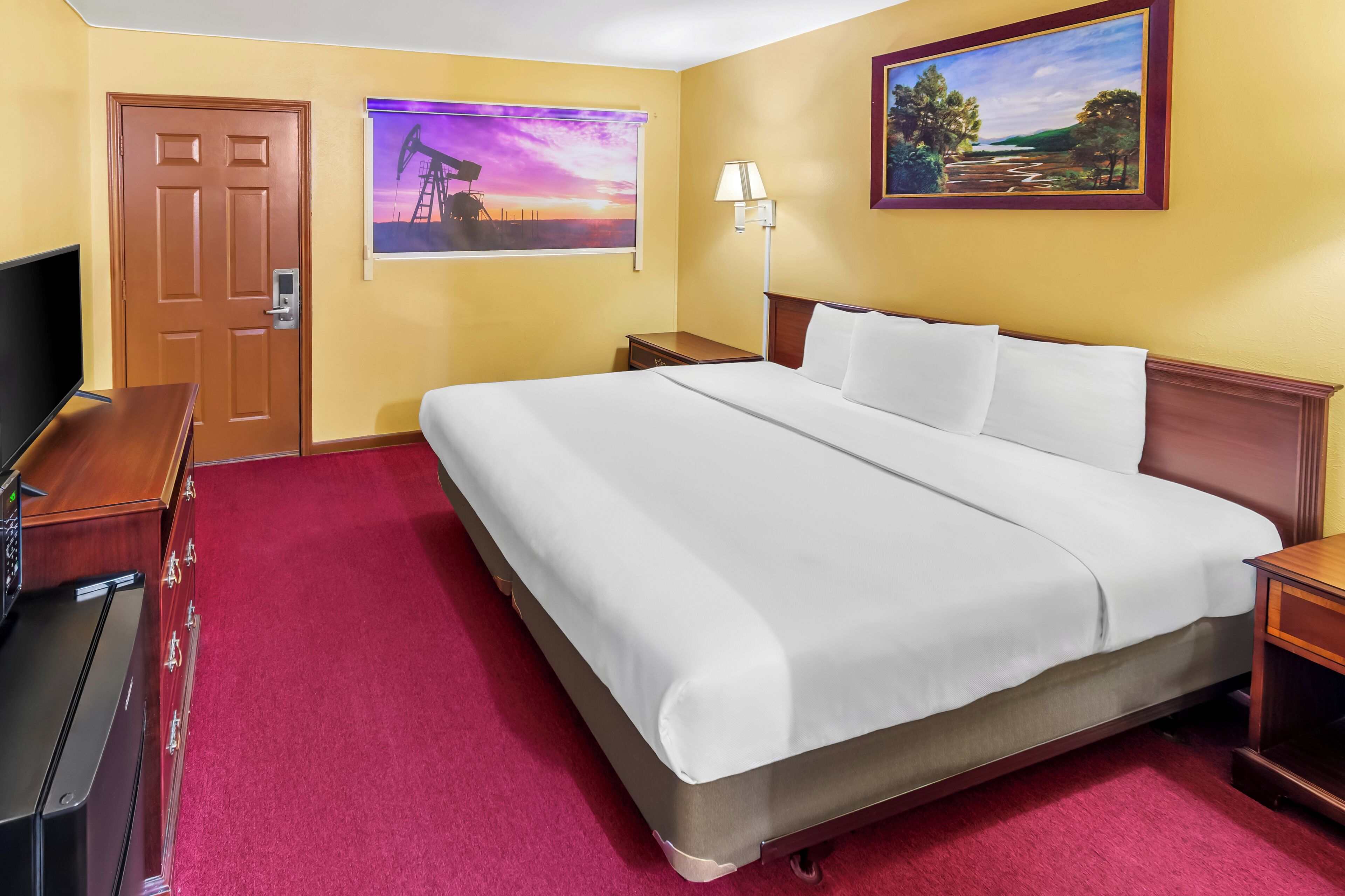 Een hotelkamer met een groot bed, een televisie, een bureau en een schilderij aan de muur.