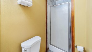 Un baño con inodoro, cabina de ducha y toallero con toallas dobladas.