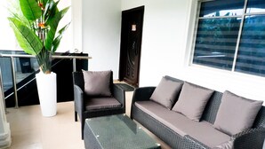 A modern lounge area with wicker furniture, a potted plant, and a view of the city through large windows. - The RiverSide Apartments - Ile Ife Nigeria (Ife)