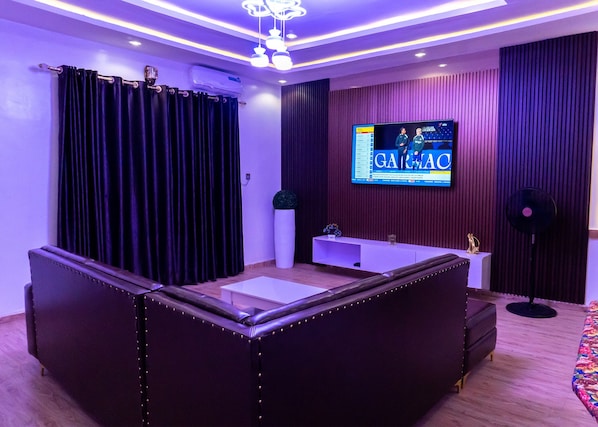 A modern living room with a sectional sofa, a flat-screen TV mounted on the wall, and a small white table.
