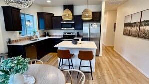 Une cuisine moderne avec des meubles de couleur sombre, un îlot central et des luminaires suspendus.
