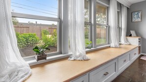 Una cocina con una encimera de madera alargada, ventanas amplias con cortinas blancas y vistas a un patio trasero.