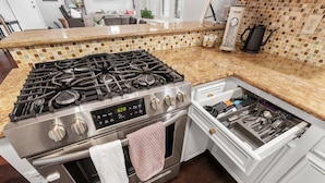 Una cocina con estufa, horno de acero inoxidable y un cajón integrado para utensilios.