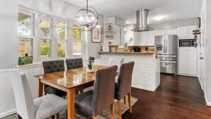 Una cocina moderna con muebles blancos, electrodomésticos de acero inoxidable y un comedor con mesa de madera y sillas tapizadas.
