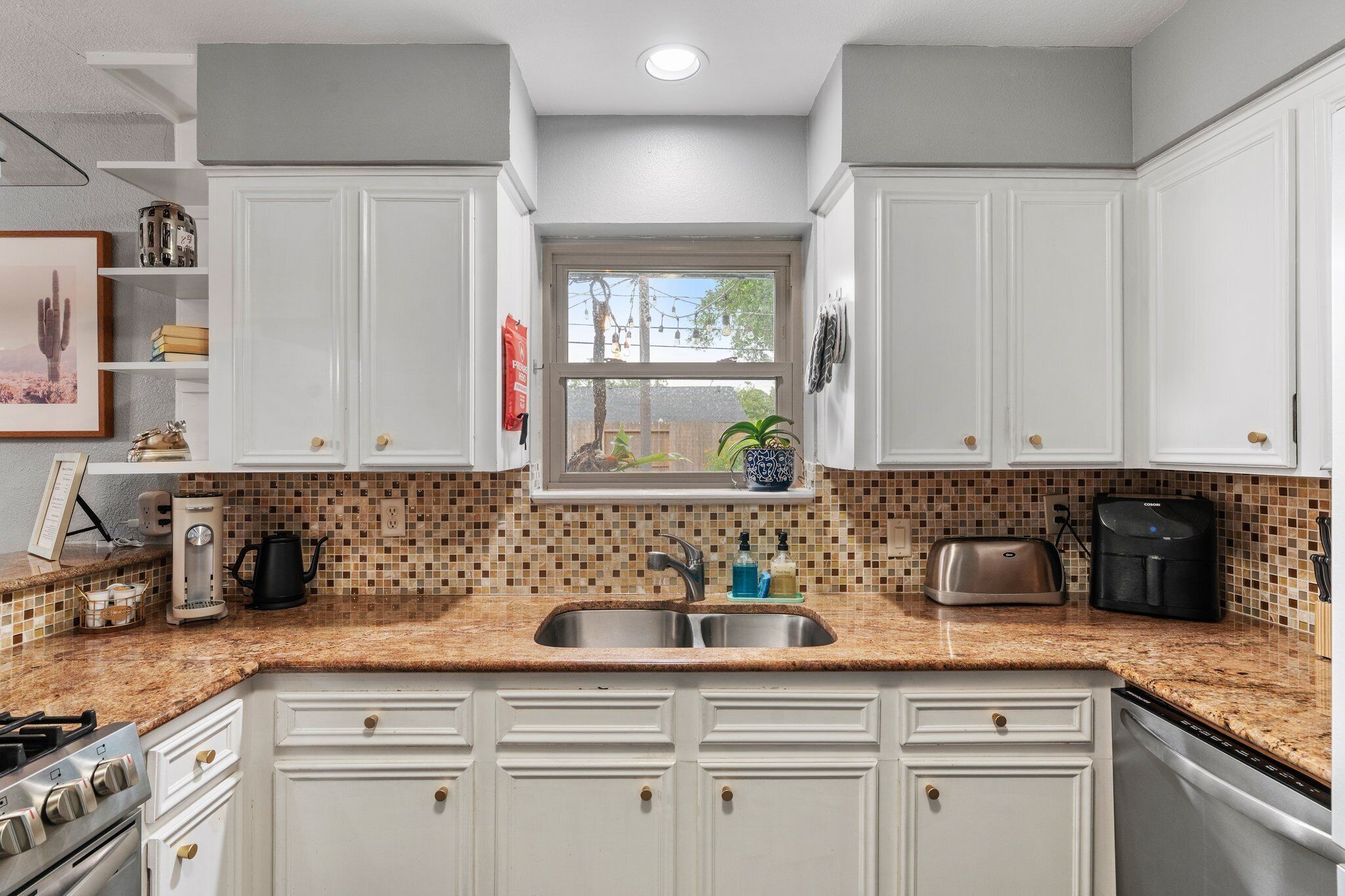 A kitchen with white cabinets, a double sink, a window, and a tiled backsplash.