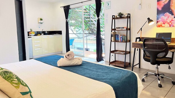 A hotel room with a bed, a desk with a laptop, a chair, a bookshelf, and a view of a swimming pool. - Ocean Lovers Taganga Dive Center& Hostel (Taganga)