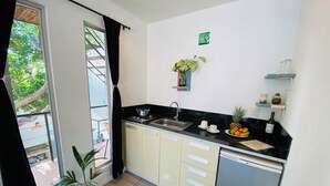 A compact kitchen with a sink, stove, and a small refrigerator. There are two potted plants, a fruit bowl, and a wine bottle on the counter. - Ocean Lovers Taganga Dive Center& Hostel (Taganga)