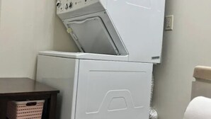 Un lavadero con lavadoras apiladas y un armario de madera oscura con una cesta.