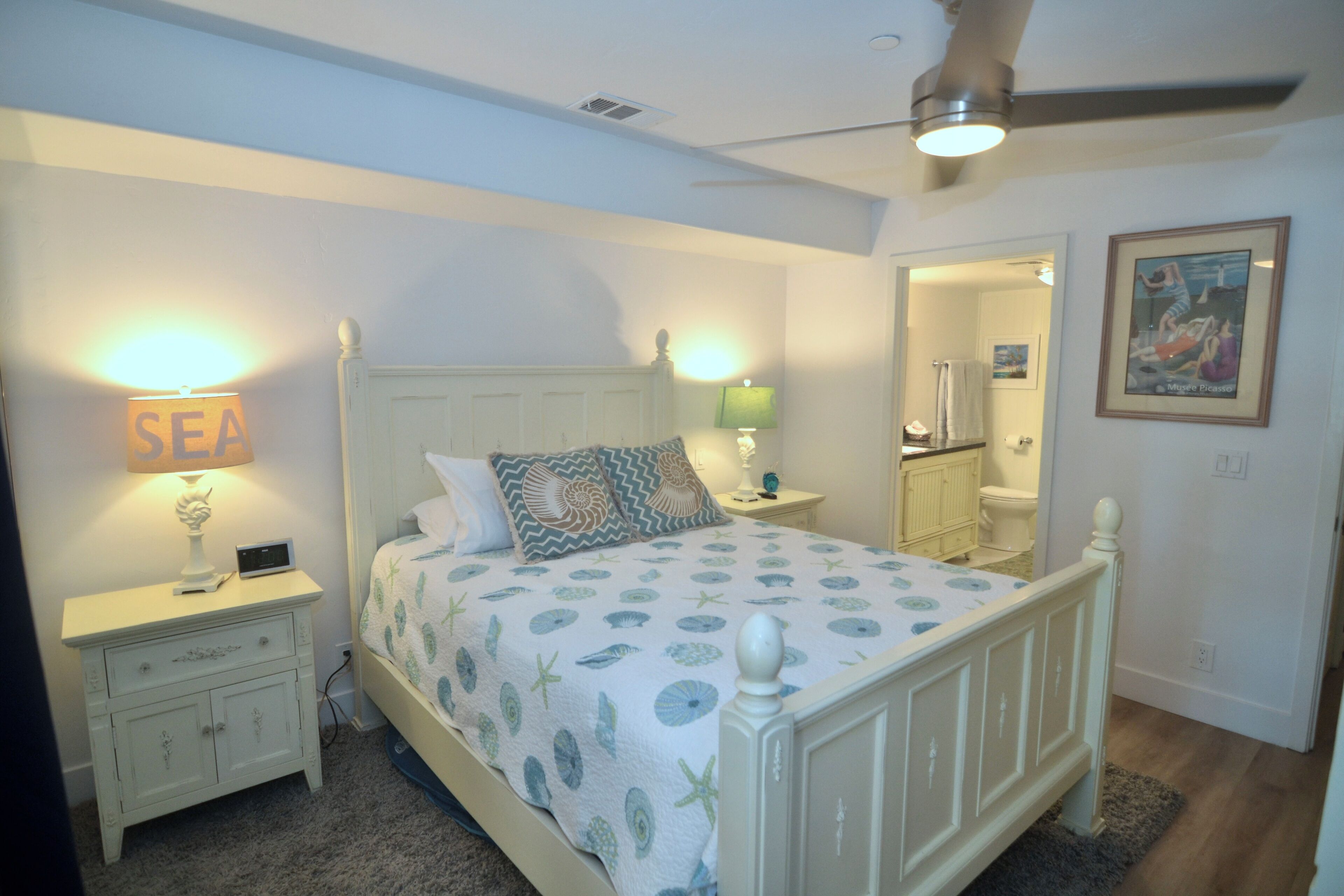 A bedroom with a bed, nightstands, a ceiling fan, and a bathroom visible through an open door.
