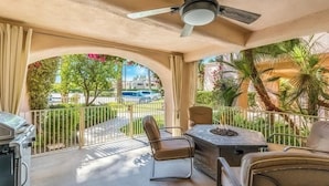 Une terrasse extérieure couverte, dotée d’un ventilateur de plafond, d’un barbecue et d’une table avec des chaises.