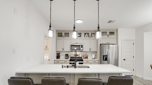 A modern kitchen with white cabinetry, a central island with bar stools, stainless steel appliances, and pendant lighting.