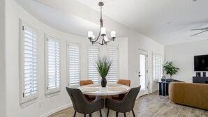 A dining area with a round table, chairs, a chandelier, and a potted plant.