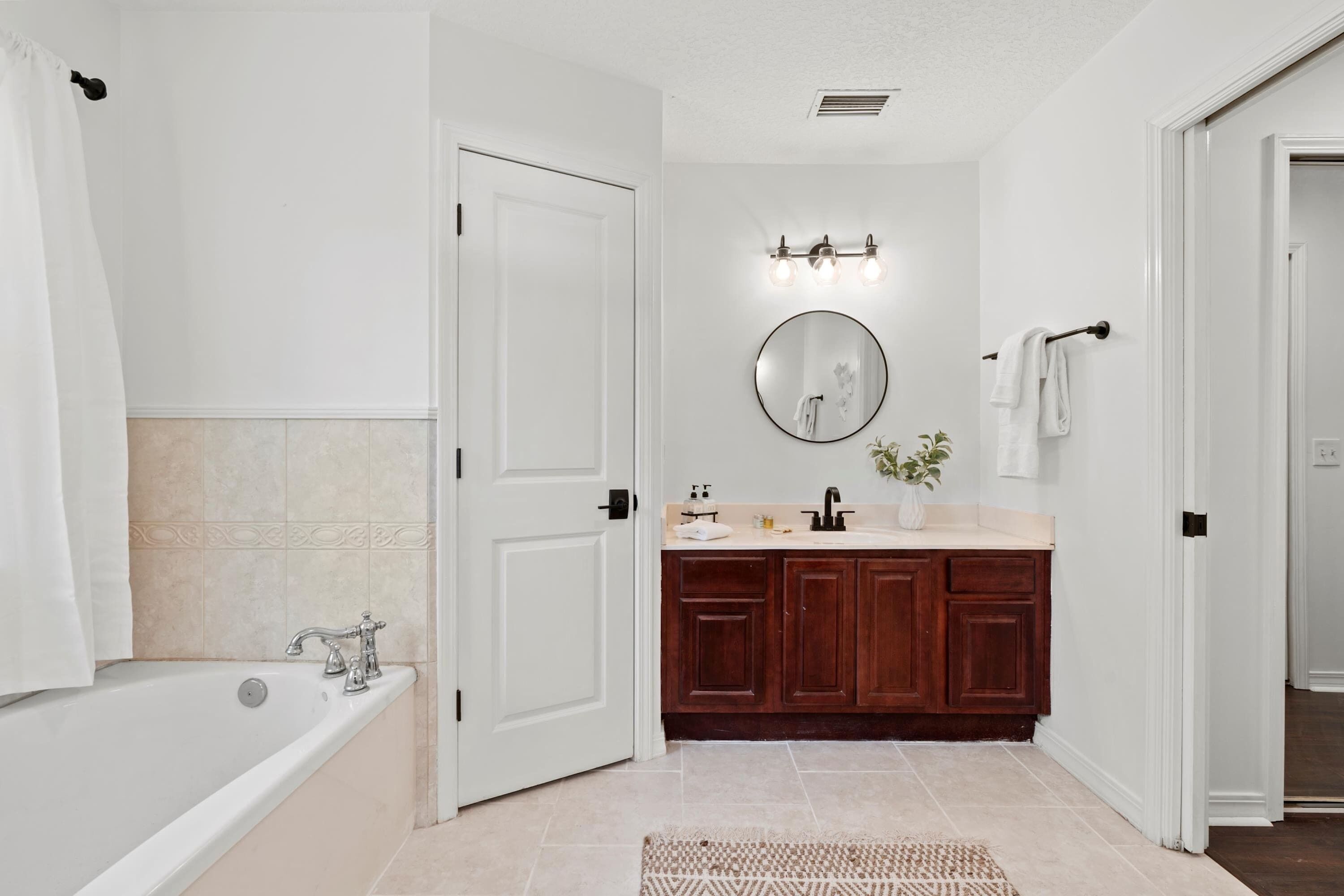A bathroom with a bathtub, a sink, a mirror, and wooden cabinets.