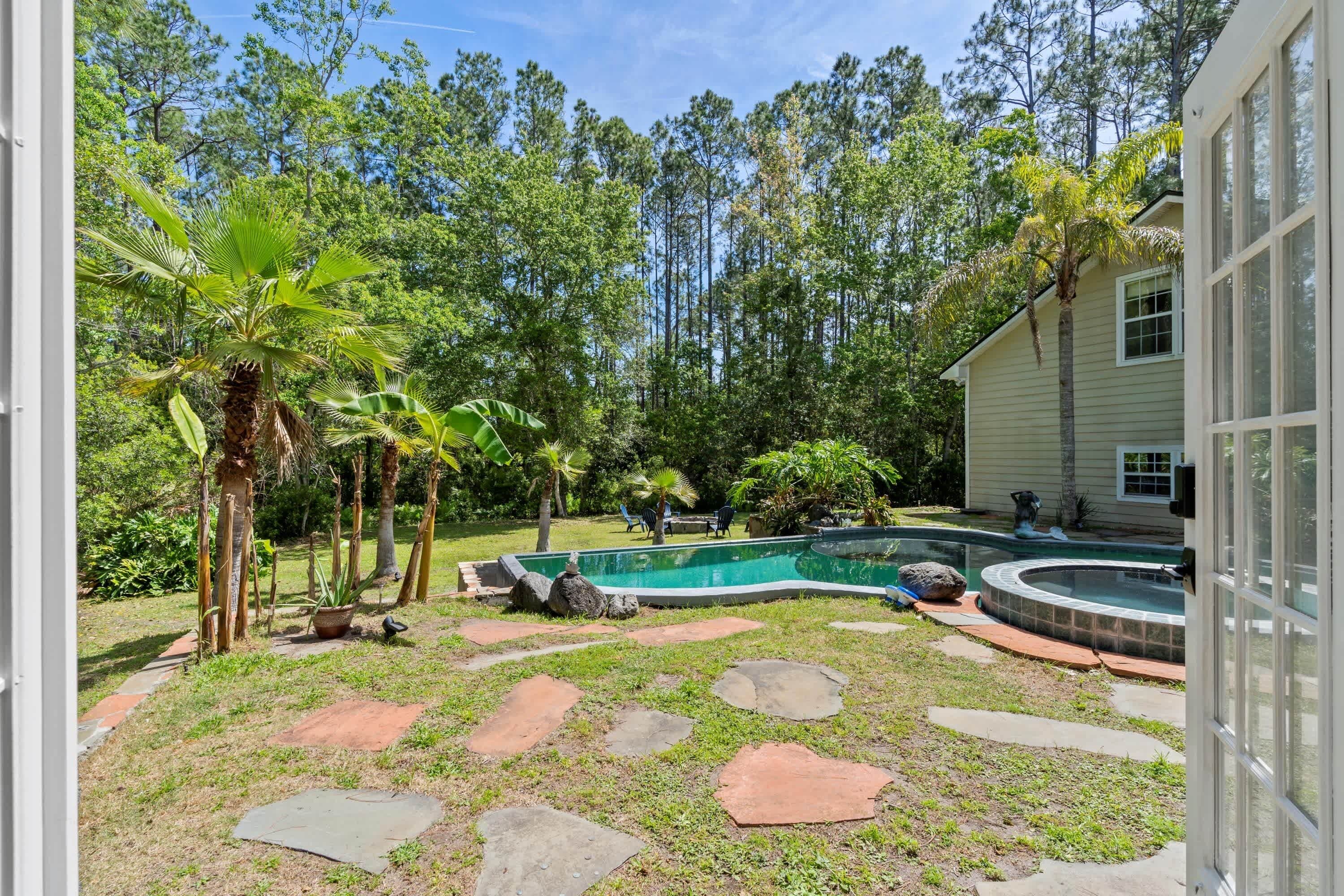 A backyard with a swimming pool, stone pathways, and tropical plants.