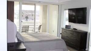 Une chambre avec un lit, une commode, une télévision et un balcon offrant une vue.