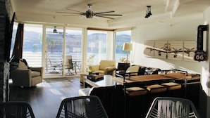 Un vaste espace de vie doté d’une grande porte-fenêtre coulissante donnant sur un balcon, d’un ventilateur de plafond, d’un coin bar avec des tabourets et d’une décoration murale représentant un avion.