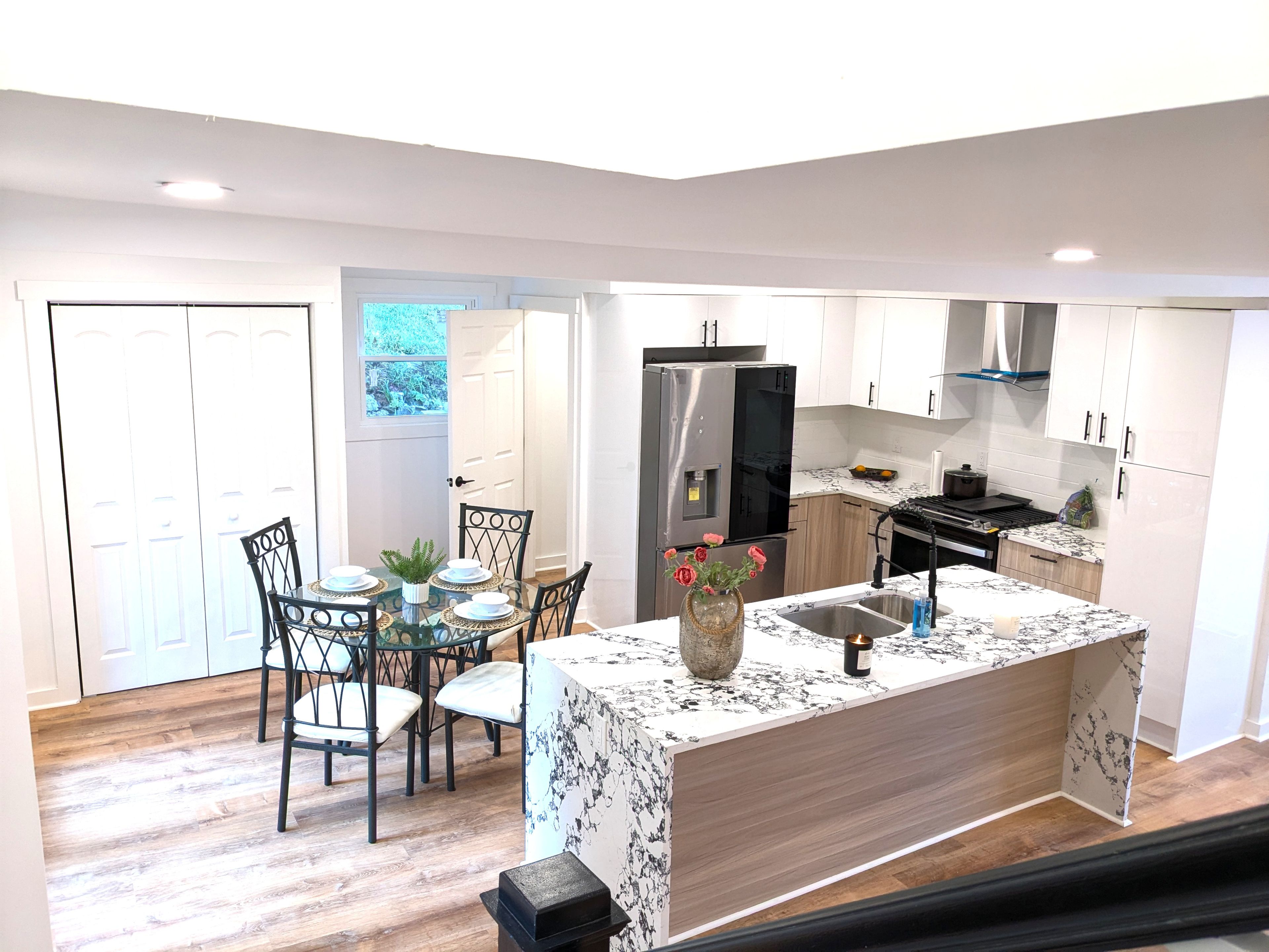 A modern kitchen with a central island, dining table with chairs, and a refrigerator.