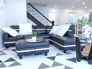 A modern living room with a sectional sofa, a glass coffee table, and a staircase.