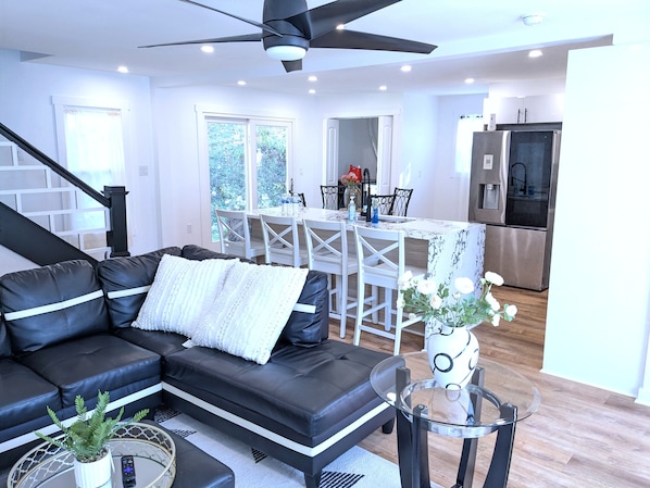 A modern living room with a sectional sofa, a glass coffee table, and a dining area with a white table and chairs.