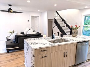 A modern kitchen with a marble countertop, wooden cabinets, a built-in dishwasher, and a black faucet.