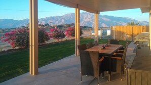 Une terrasse extérieure avec une table et des chaises, un barbecue et une vue sur les montagnes et les fleurs roses.