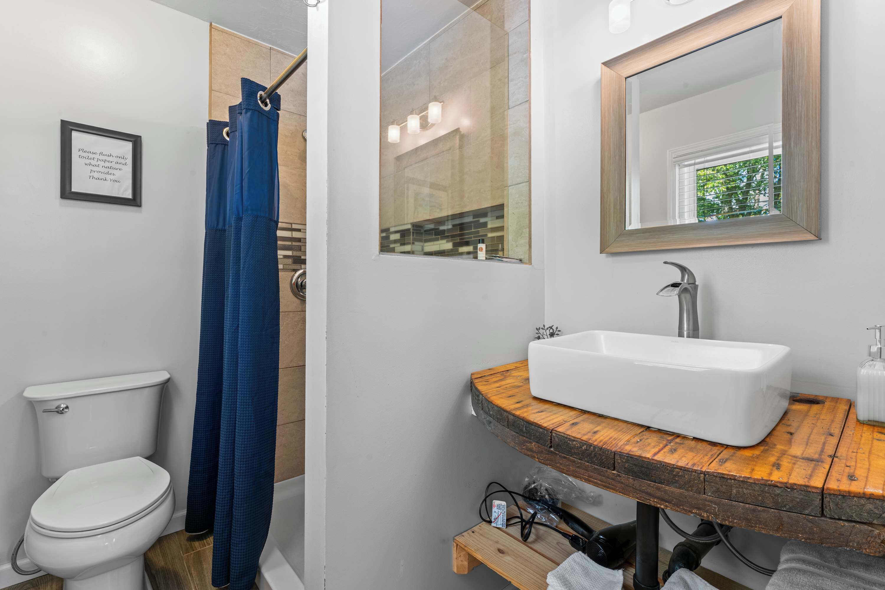 A bathroom with a white toilet, a shower with a blue curtain, a wooden vanity with a white sink, and a mirror above the sink.