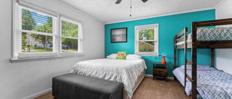 A bedroom with a bed, a bench, a ceiling fan, and a window with blinds.