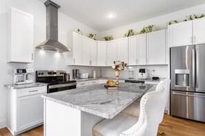 A modern kitchen with white cabinetry, a central island, stainless steel appliances, and decorative plants. - Royal Nash Penthouse Downtown Luxury Stay (Nashville)