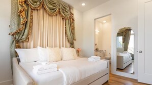A spacious bedroom with a large bed, a mirror, and a view of the bathroom.