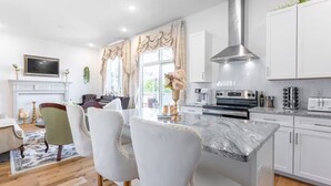 A modern kitchen with white cabinetry, a stainless steel range hood, and a marble countertop.