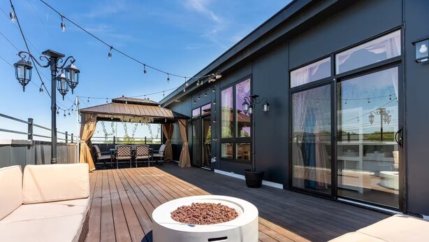 A rooftop deck with outdoor seating, a fire pit, and string lights.
