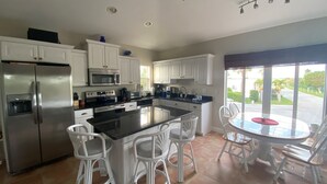 A modern kitchen with white cabinets, stainless steel appliances, and a central island with bar stools. - 4BR House in Ocean Resort w/ Private Beach, Pool, Pickleball, Marina, and More! (Jensen)