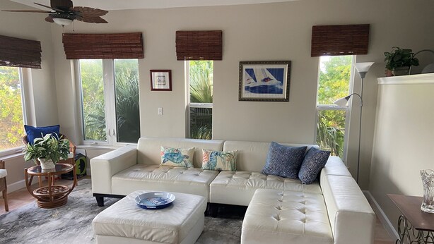 A living room with a white sectional sofa, a round coffee table, and a patterned rug. There are windows with blinds, a ceiling fan, and a framed picture on the wall. - 4BR House in Ocean Resort w/ Private Beach, Pool, Pickleball, Marina, and More! (Jensen)
