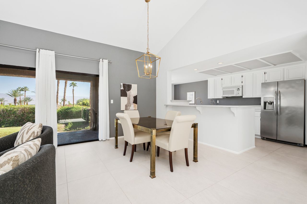A modern kitchen with white cabinets, a stainless steel refrigerator, and a dining area with a glass table and white chairs.