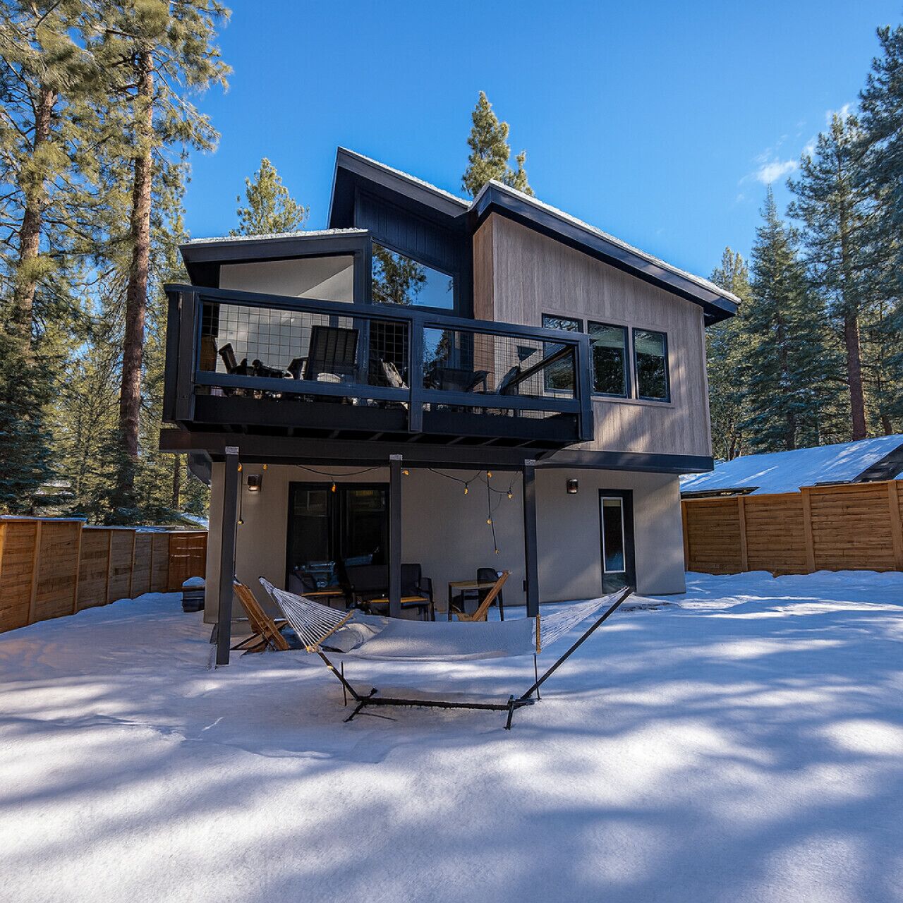 A modern two-story house with a balcony, a hammock, and a snow-covered yard.