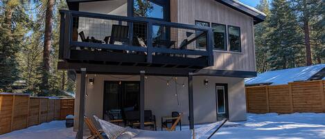 A modern two-story house with a balcony, a hammock, and a snow-covered yard.