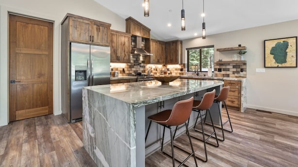 Une cuisine moderne dotée d’un grand îlot central, de meubles en bois, d’appareils électroménagers en acier inoxydable et de luminaires suspendus.