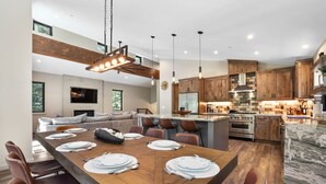 Une cuisine moderne avec des meubles en bois, un grand îlot central et un coin repas doté d’une longue table pouvant accueillir six personnes.