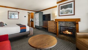Una habitación de hotel con una cama, un aparador de madera, una mesa redonda de madera, una chimenea y un televisor.