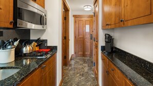 Una cocina estrecha con armarios de madera, microondas de acero inoxidable, cafetera y estufa con utensilios.