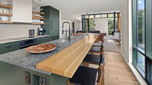 Una cocina moderna con una amplia encimera de madera, electrodomésticos integrados y un gran ventanal con vistas al exterior.