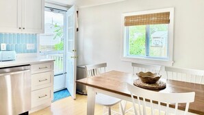 Une cuisine avec des meubles blancs, une table en bois et une fenêtre donnant sur un paysage verdoyant.