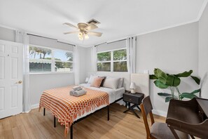 A bedroom with a bed, bedside table, lamp, chair, and a ceiling fan.