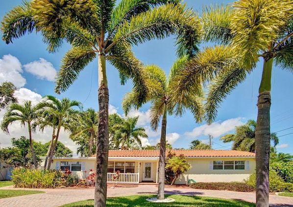 A single-story house with a tiled roof, surrounded by palm trees and a well-maintained lawn.