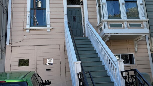 A two-story building with a front entrance, a staircase with a black railing, and a green car parked in front. - Jersey Street Gem: Charming 1 Bedroom 1Bathroom (San Francisco)