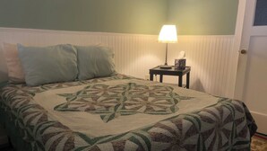 A bed with a patterned quilt, two pillows, a bedside lamp, and a small table with a vase. - Jersey Street Gem: Charming 1 Bedroom 1Bathroom (San Francisco)