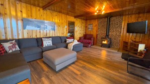 Un intérieur de chalet chaleureux avec un canapé d’angle, un pouf et une cheminée.